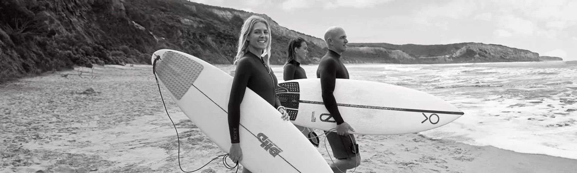 {generated} Tres surfistas con tablas esperan en una costa tranquila, transmitiendo un ambiente aventurero ideal para inscripciones al boletín.