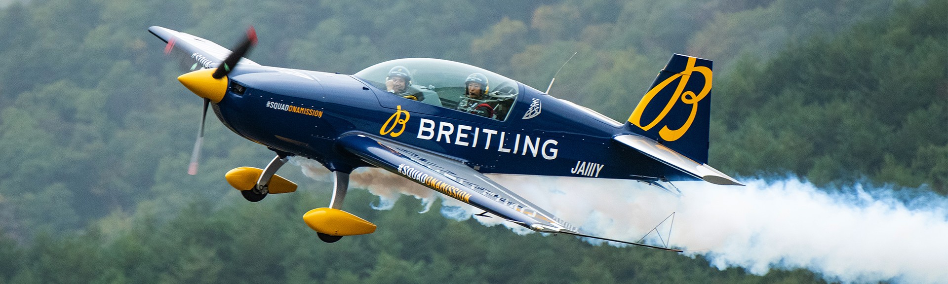 {generated} Breitlingロゴを配した曲技飛行機が煙の軌跡を描き森林背景を背に飛行する様子を捉えた動的なシーン