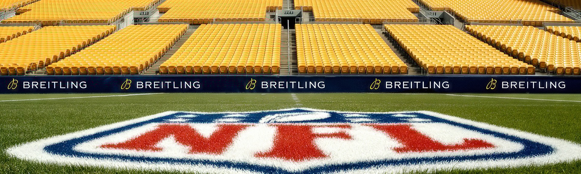 {generated} NFL pitch with bold midfield logo framed by empty yellow stands and clear Breitling branding along the touchlines.