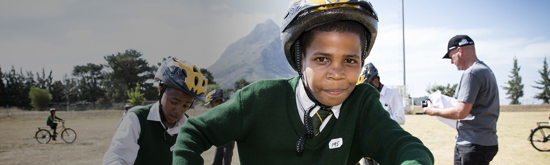 {generated} Des élèves casqués roulent à vélo en plein air dans le cadre de l’initiative Breitling x Qhubeka devant un décor montagneux.