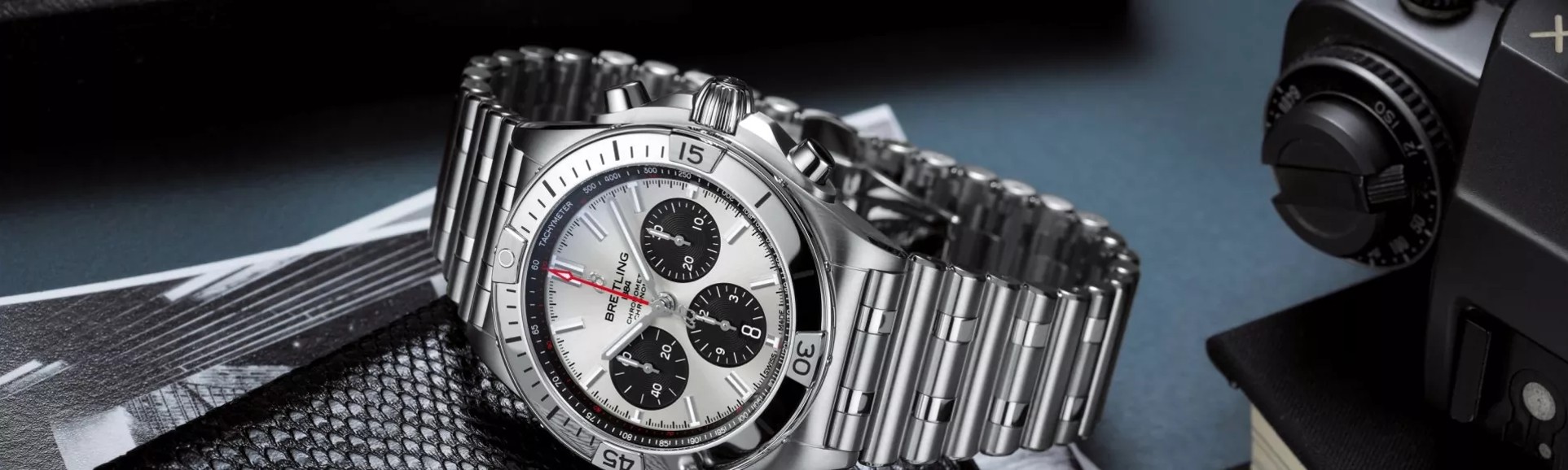 {generated} Полированный стальной хронограф Breitling Chronomat рядом с винтажной камерой, подчёркивая выразительный циферблат и браслет.