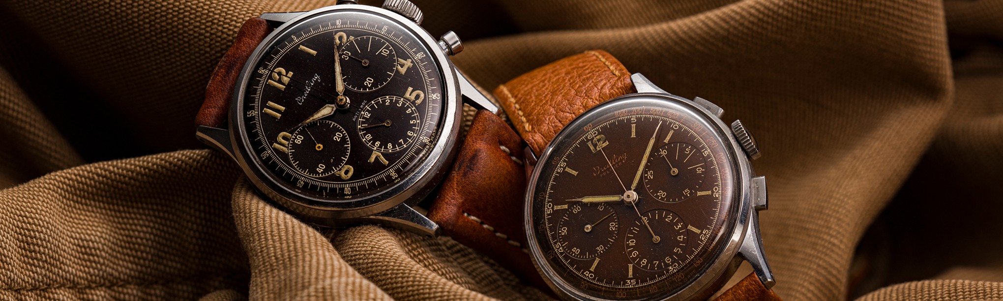 {generated} Two vintage Breitling Premier chronographs with dark dials and leather straps displayed against textured brown fabric.