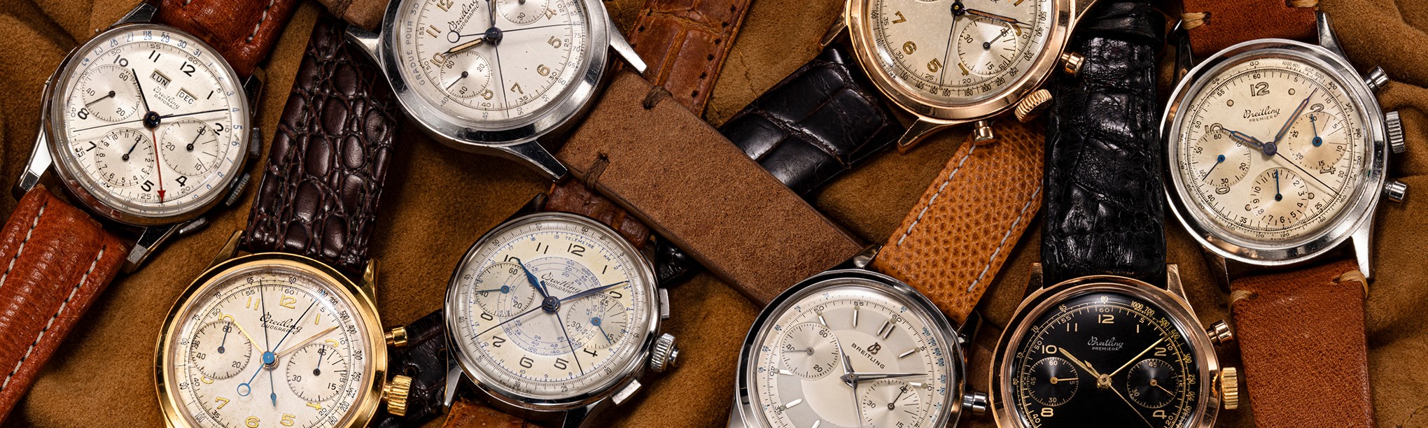 {generated} Vintage Breitling Premier chronographs arranged on soft tan fabric, showing varied dials and leather straps