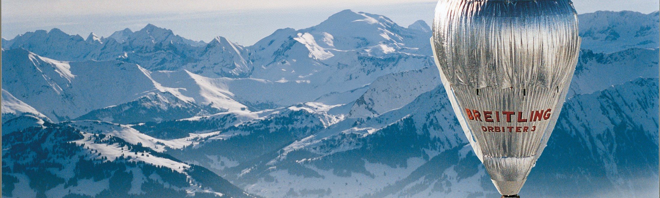 {generated} Breitling Orbiter 3 hot-air balloon gliding above expansive snowy mountain peaks, highlighting adventurous spirit.