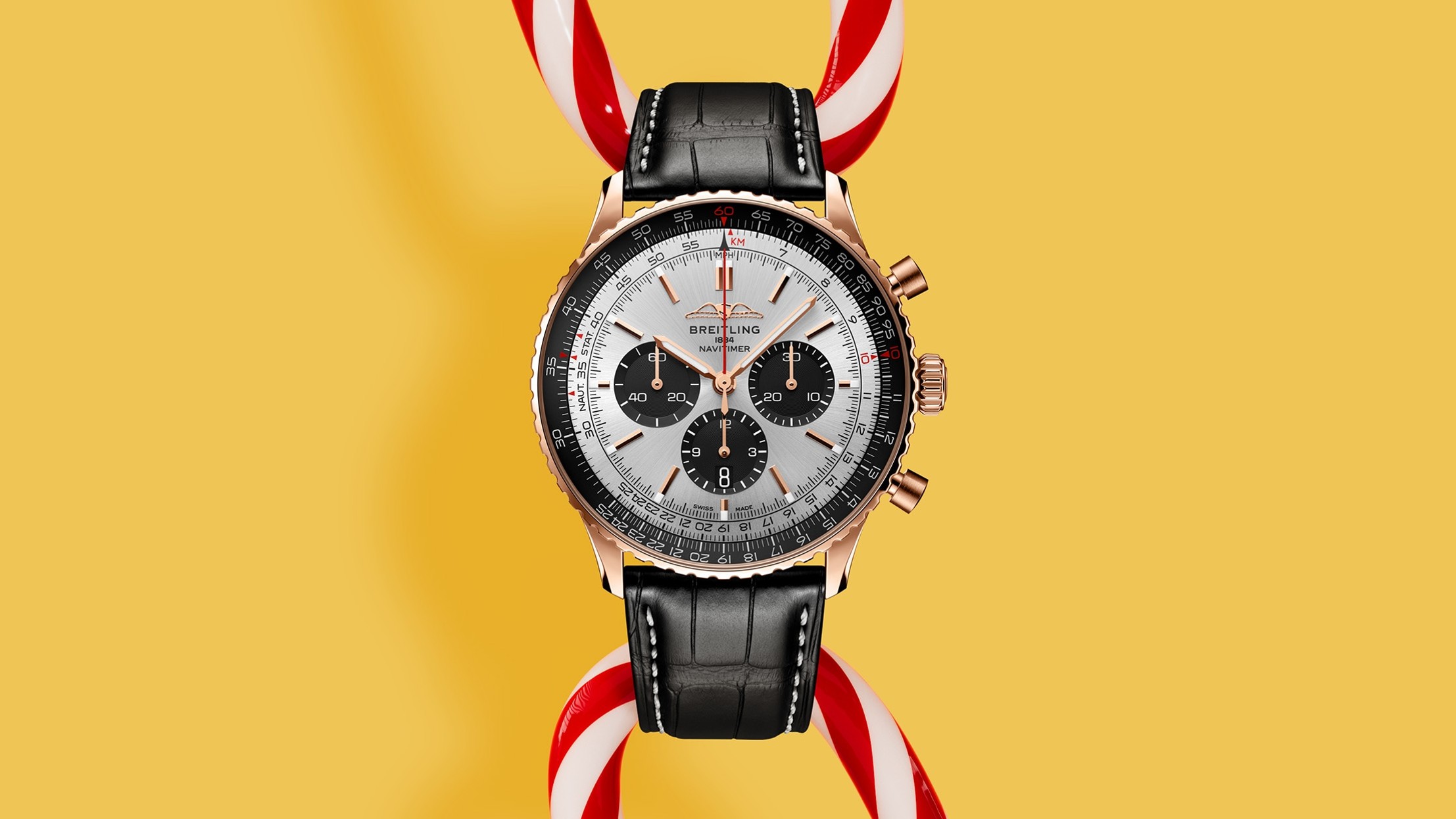 Breitling Navitimer chronograph with rose gold case, white dial, black subdials, and black leather strap against yellow background with candy cane decoration.