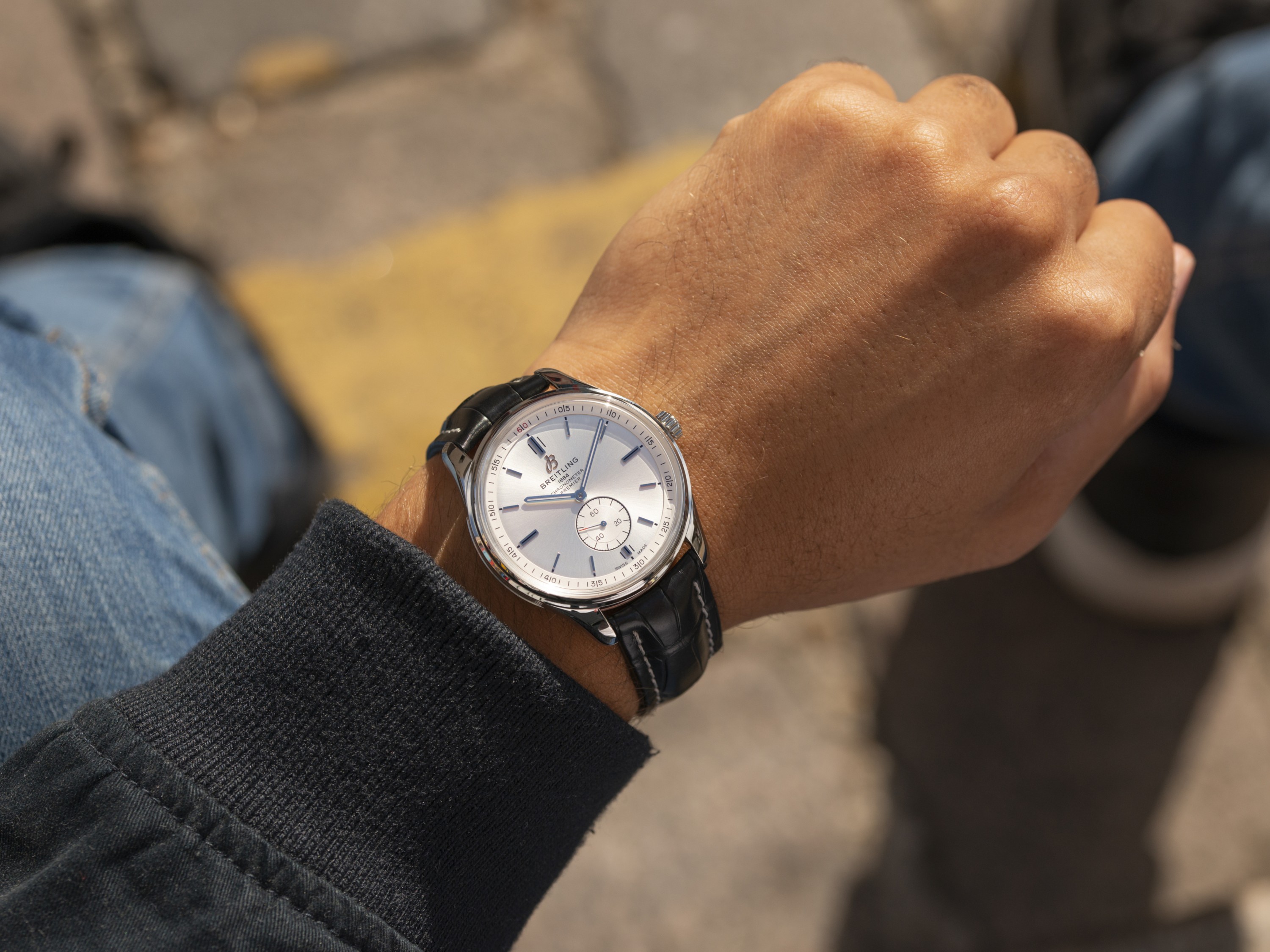 {generated} 在自然街道光線下呈現一隻配戴銀色錶盤與黑色皮錶帶Breitling腕錶的手腕
