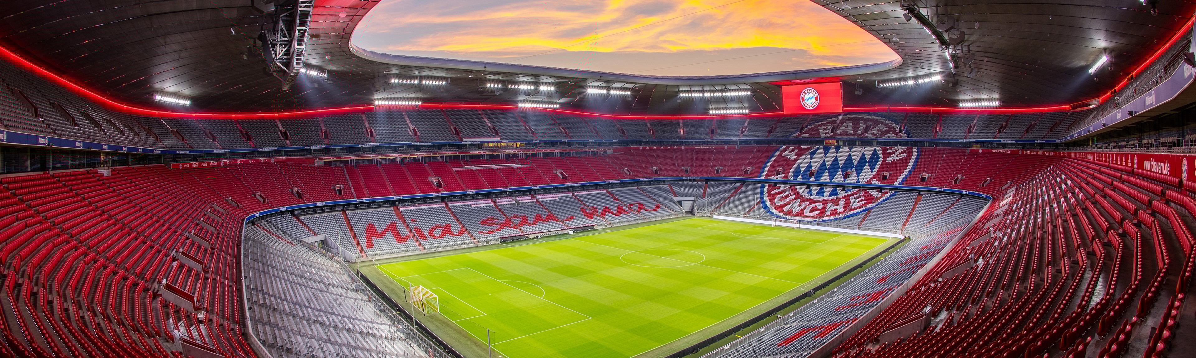 {generated} 夕陽下的拜仁球場全景，空蕩看台的紅色座椅與俱樂部徽章映襯中央的綠色球場