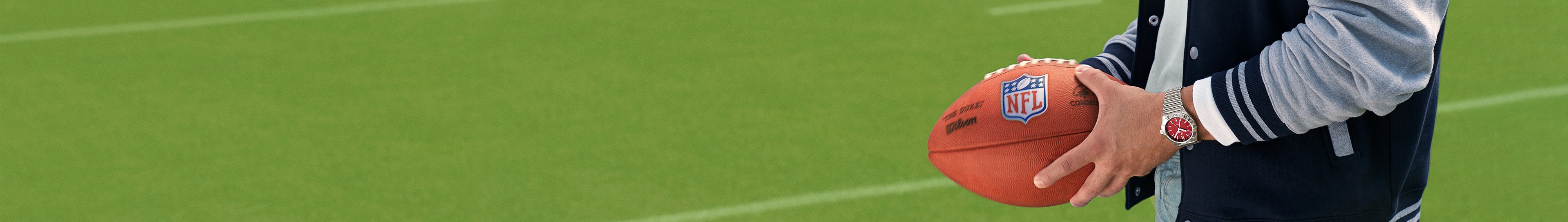 {generated} Una persona sostiene un balón NFL en un campo verde mientras luce un reloj Breitling de esfera roja en un ambiente deportivo.