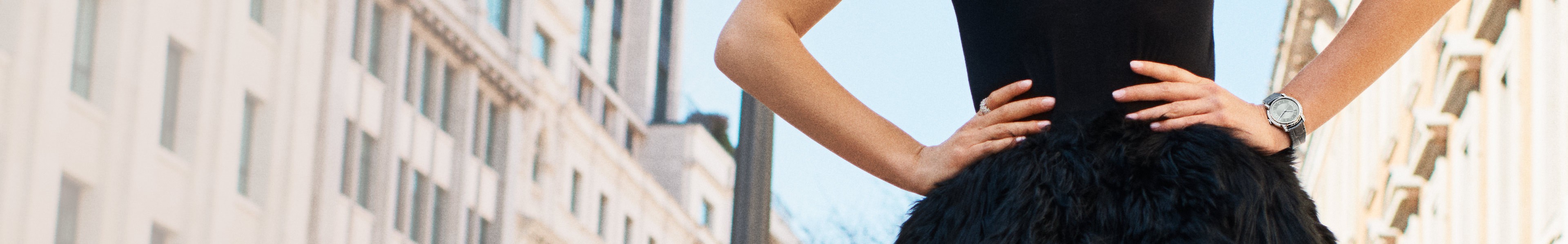 {generated} A woman poses in a black dress, showcasing a Breitling Lady Premier watch against an elegant city backdrop