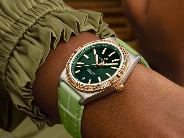 {generated} Poignet féminin en tons pastel mettant en valeur une montre Breitling à cadran vert, lunette sertie et bracelet assorti.