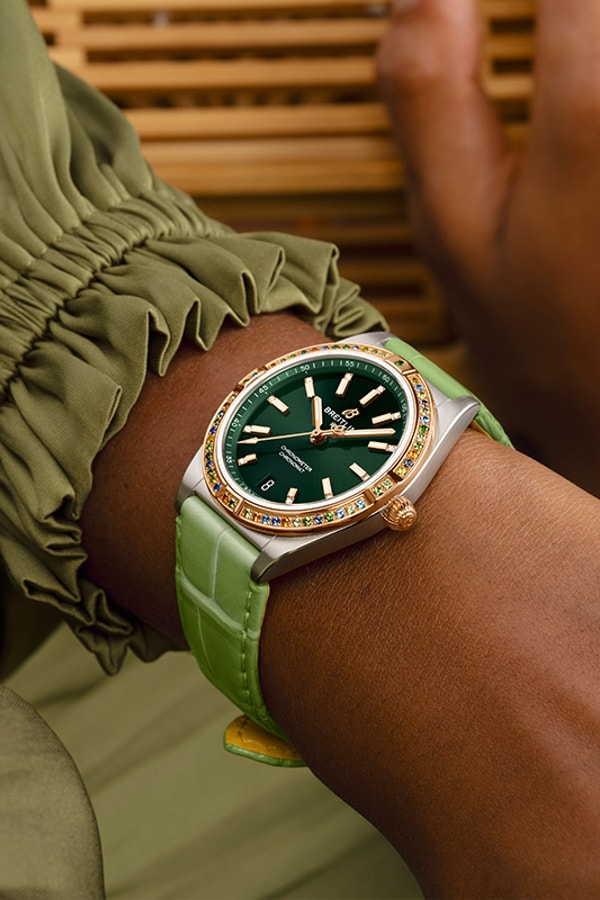{generated} Poignet féminin en tons pastel mettant en valeur une montre Breitling à cadran vert, lunette sertie et bracelet assorti.