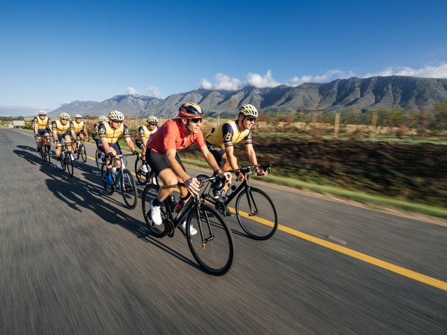 {generated} L’équipe de triathlon Breitling avance en formation sur une route ensoleillée, affichant une détermination sportive face aux montagnes.