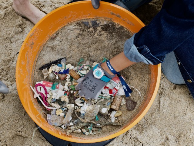 {generated} A volunteer sorts beach debris through a sieve, wearing a Breitling watch as part of a sustainability-focused partnership.