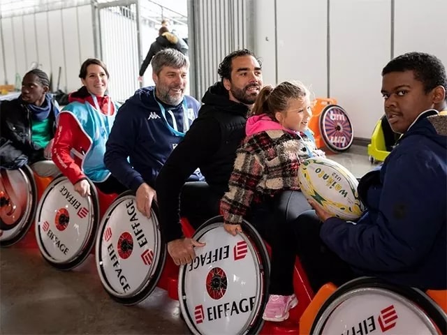 {generated} Enfants et adultes avancent sur des chariots colorés en intérieur lors d’une activité Premiers de cordée, partageant un moment convivial.