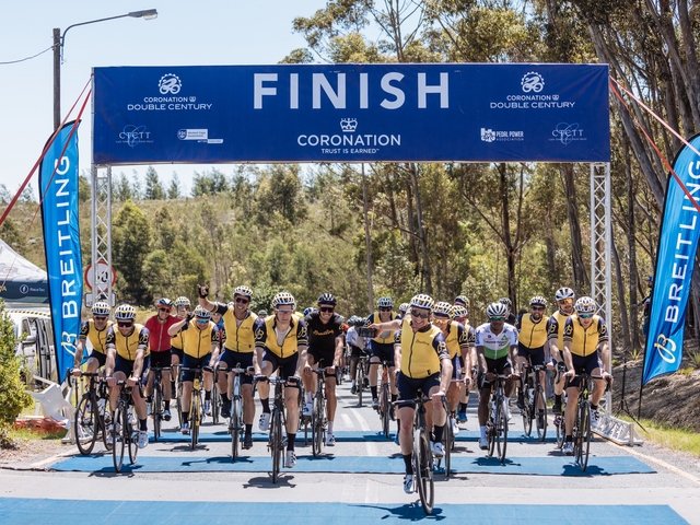 {generated} Des cyclistes en maillots jaunes franchissent la ligne d’arrivée avec un marquage Breitling visible, soutenant la mission Qhubeka