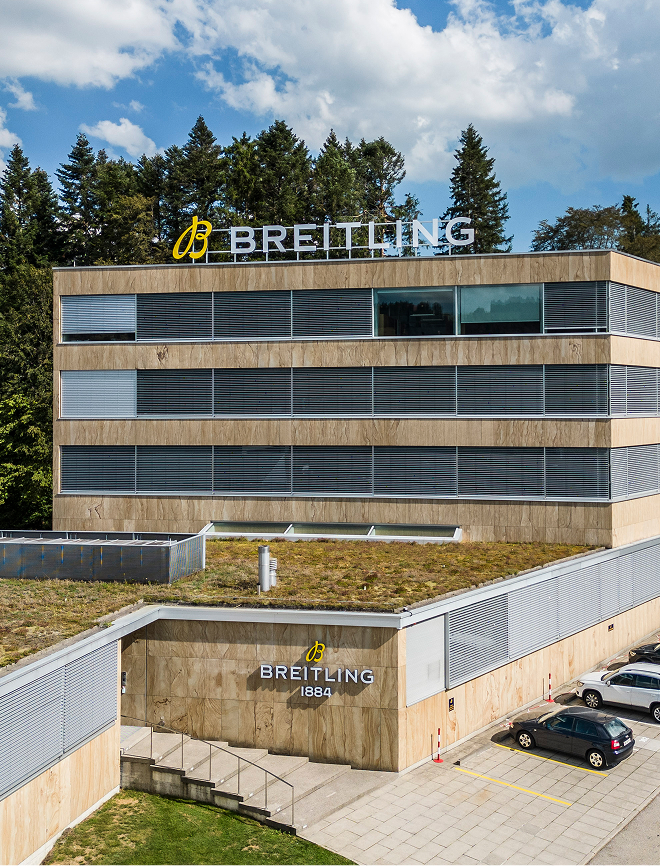 {generated} 被樹木環繞的百年靈現代多層建築，醒目標誌展現品牌獨特的建築風格