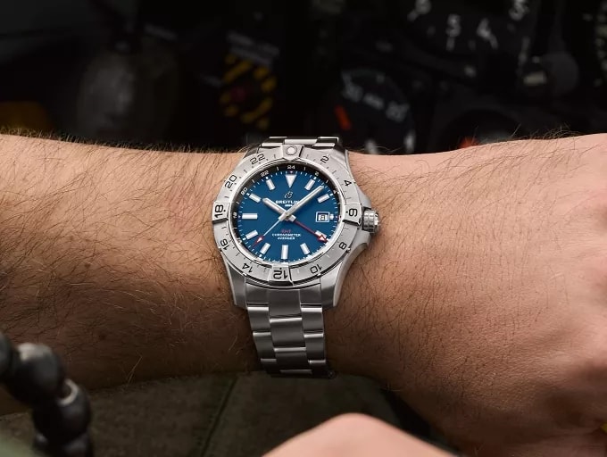 {generated} 配備藍色錶盤的Breitling Avenger Automatic GMT 44佩戴於腕間，以座艙儀表為背景展現其航空設計風格。