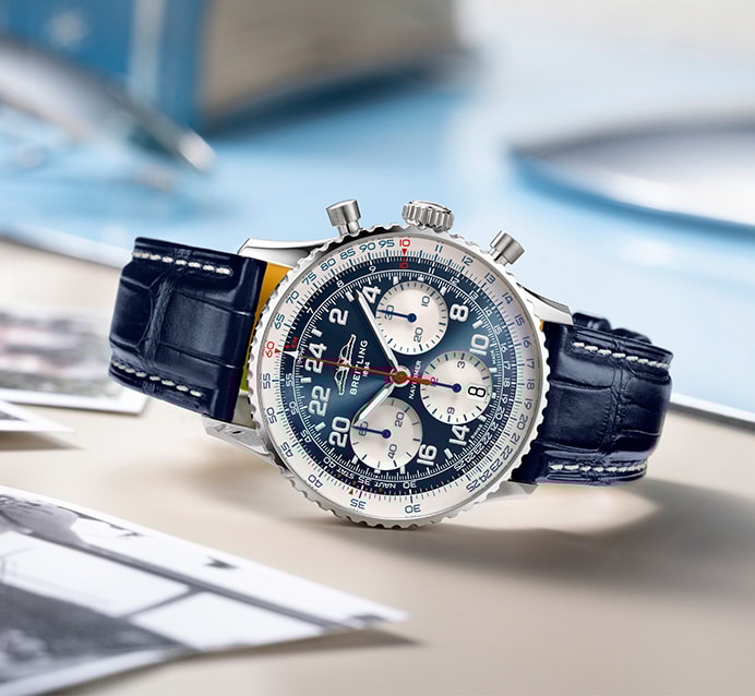{generated} ブルー文字盤とレザーストラップのBreitling Scott Carpenter Centenaryが机上のヴィンテージ写真と共に置かれている