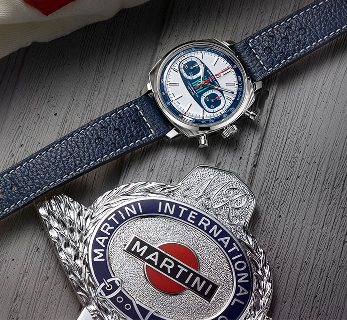 {generated} Breitling Top Time Martini Racing watch with blue strap displayed beside a polished Martini racing emblem on wood