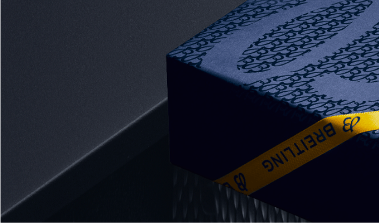 {generated} Dunkle Szene mit einer blauen Breitling‑Geschenkbox samt charakteristischem Muster und gelbem Breitling‑Band.