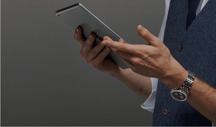 {generated} Smartly dressed advisor holding a tablet, highlighting a Breitling watch on his wrist against a refined grey background.