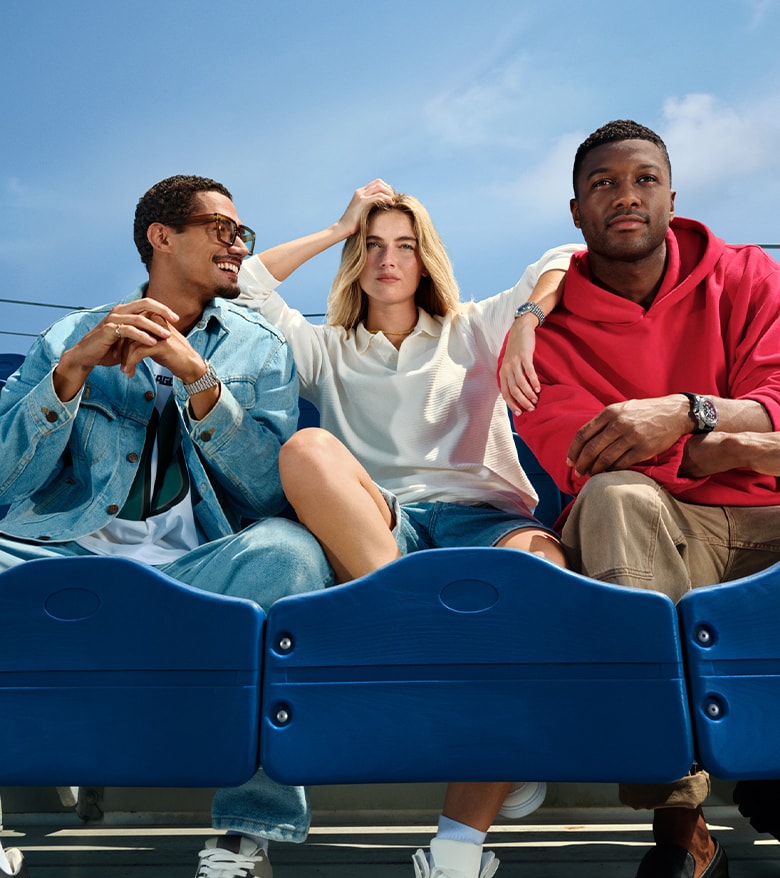 {generated} Three friends relax in bright blue stadium seats, each showcasing a Breitling watch in a casual NFL-inspired setting.