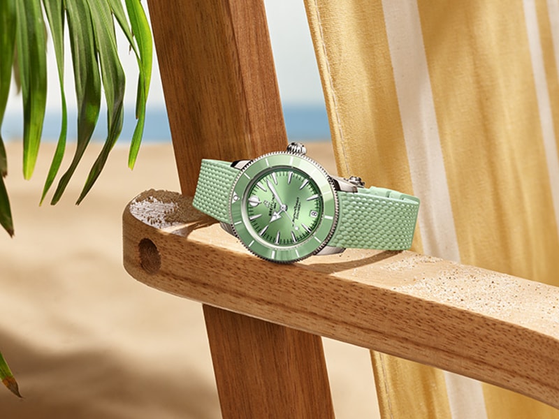 Vier verschiedenfarbige Superocean Heritage-Uhren liegen auf einem braunen Stofftuch.