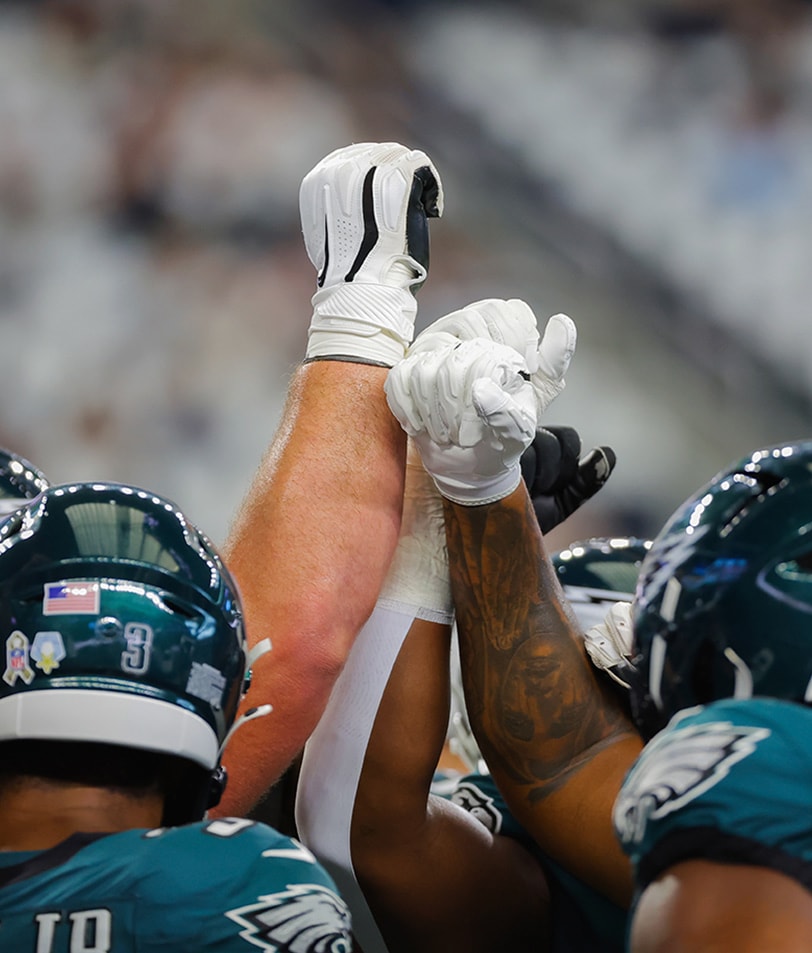 {generated} NFL players in green helmets raise gloved hands together in a tight huddle, capturing team unity and match‑day energy.
