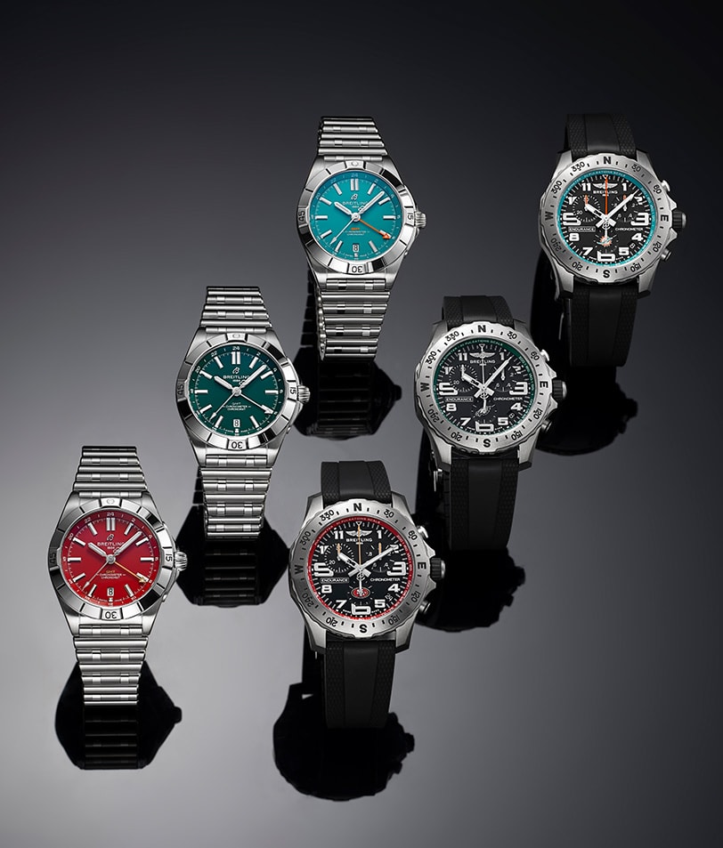 {generated} A lineup of Breitling watches with colourful dials and robust bezels presented against a dark reflective backdrop.
