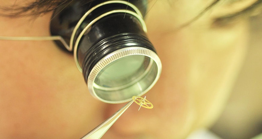 {generated} Watchmaker examining a tiny Breitling movement component with a loupe and tweezers during precise part replacement.