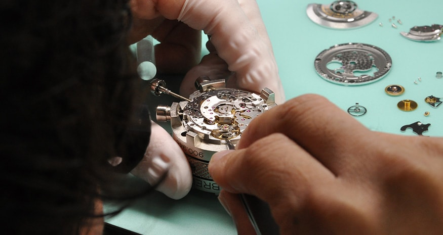 {generated} A watchmaker carefully overhauls a Breitling movement, aligning intricate components with precision tools on the workbench.