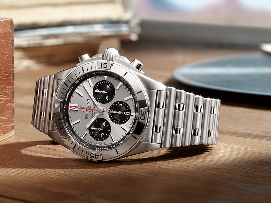 {generated} Breitling Chronomat sobre una superficie de madera, destacando su caja de acero, brazalete metálico y esfera plateada.