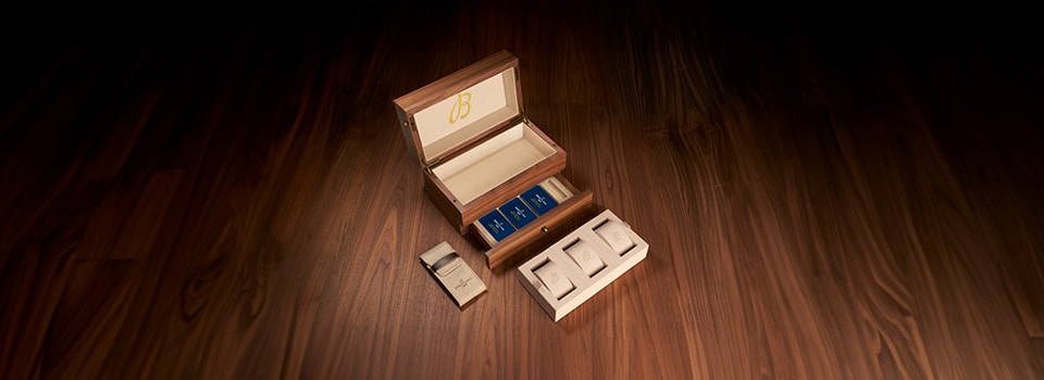 {generated} Open Breitling watch box set on polished wood, revealing cream-lined compartments and neatly arranged blue booklets.