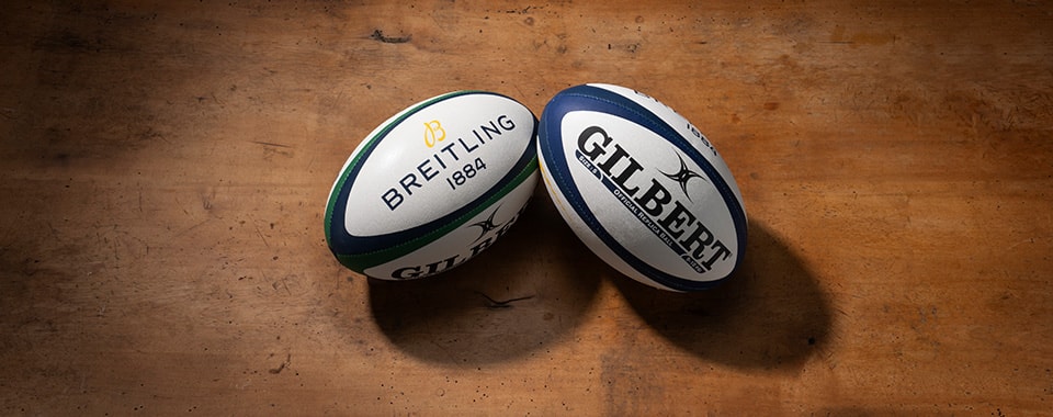 {generated} Two branded rugby balls, including a Breitling‑marked ball, placed on a wooden surface evoking the Six Nations 2025