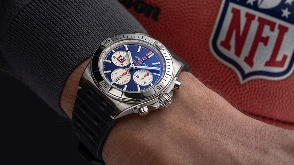 {generated} Cronógrafo Breitling com detalhes dos New York Giants no pulso ao lado de uma bola da NFL, destacando o design da equipe.