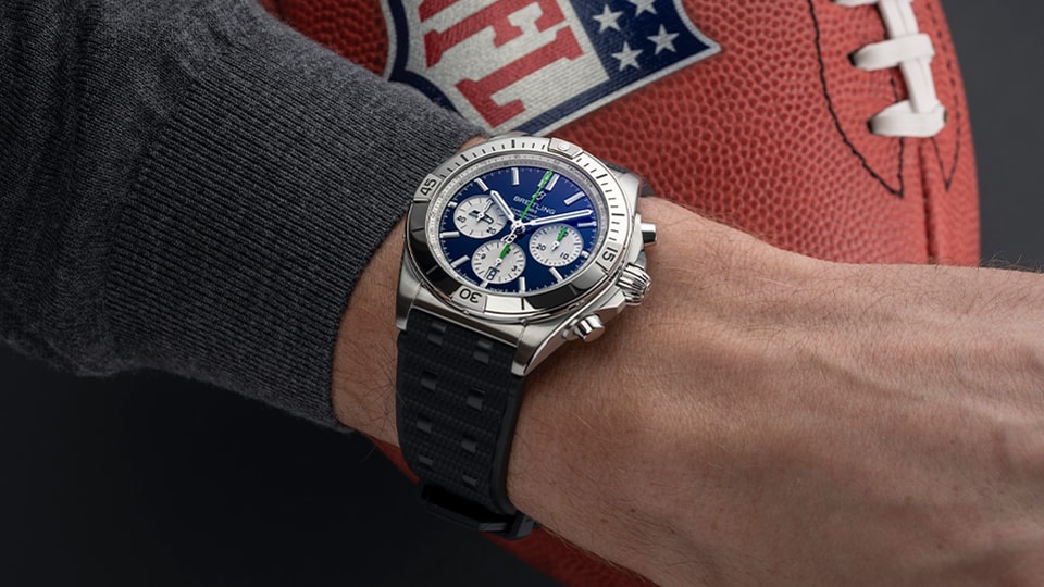 {generated} Breitling Chronomat with blue dial on a wrist beside a Seahawks-themed football, highlighting sporty precision style