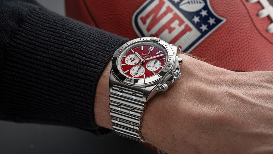 {generated} A wrist wearing a red-dial Breitling Chronomat beside an NFL football highlights the Tampa Bay Buccaneers themed design