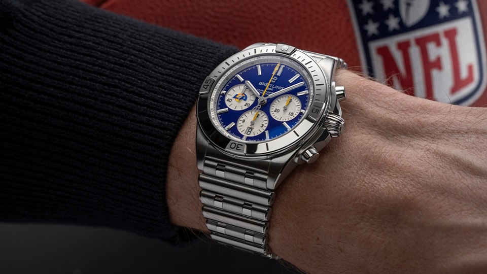 {generated} 配有藍色錶盤與洛杉磯公羊元素的Breitling腕錶在NFL橄欖球旁呈現