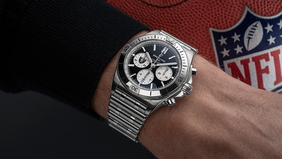 {generated} Breitling Chronomat no pulso ao lado de uma bola da NFL dos Las Vegas Raiders, destacando seu refinado design em aço polido