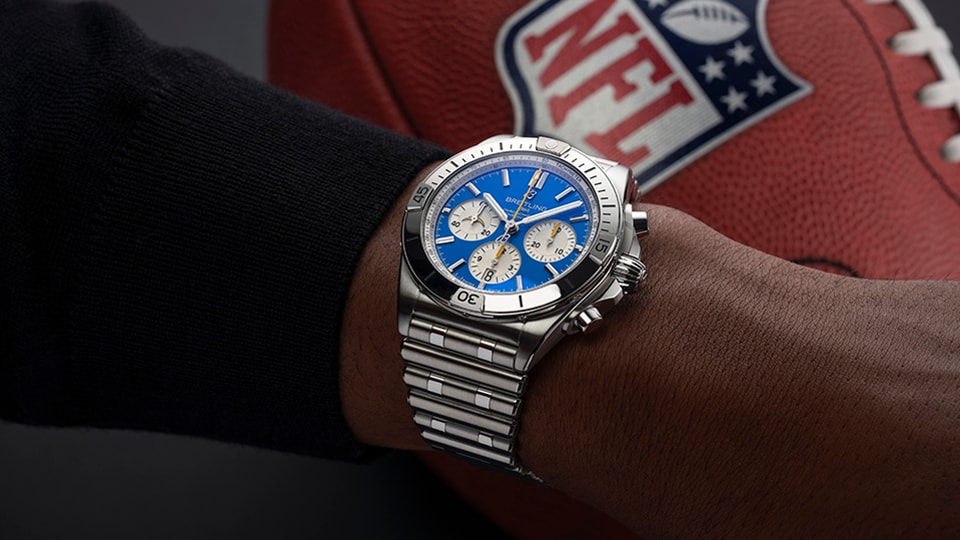 {generated} Breitling Chronomat com mostrador azul no pulso ao lado de uma bola da NFL, refletindo o tema dos Los Angeles Chargers.