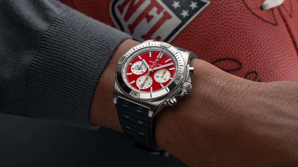 {generated} Breitling Chronomat Kansas City Chiefs edition on wrist, featuring red dial and steel case beside NFL football backdrop