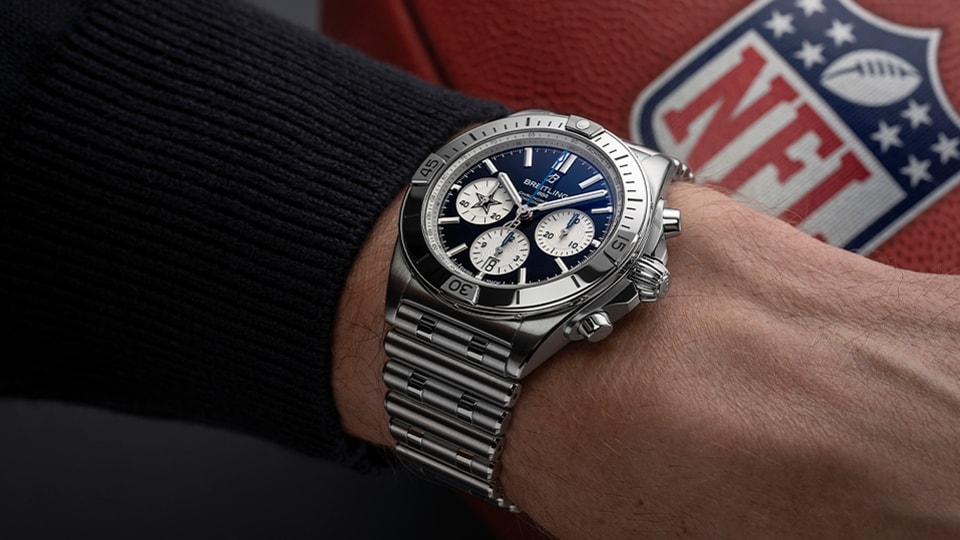 {generated} A wrist wearing a Breitling Chronomat with a blue dial set against an NFL football, highlighting sport-inspired luxury style.