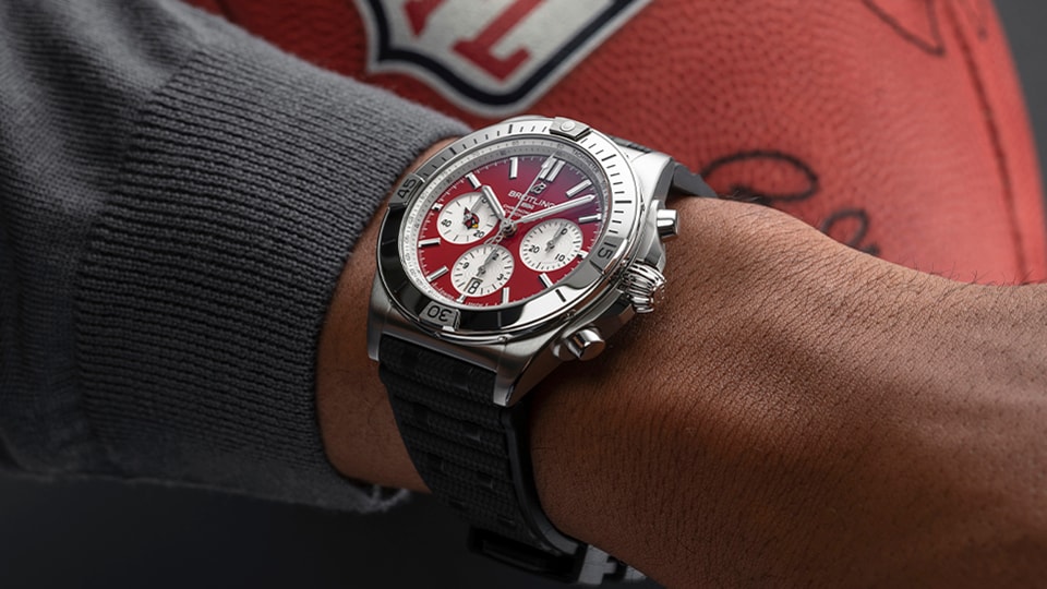 {generated} Breitling Chronomat with Arizona Cardinals red dial worn on a man’s wrist beside a textured football for team‑inspired style