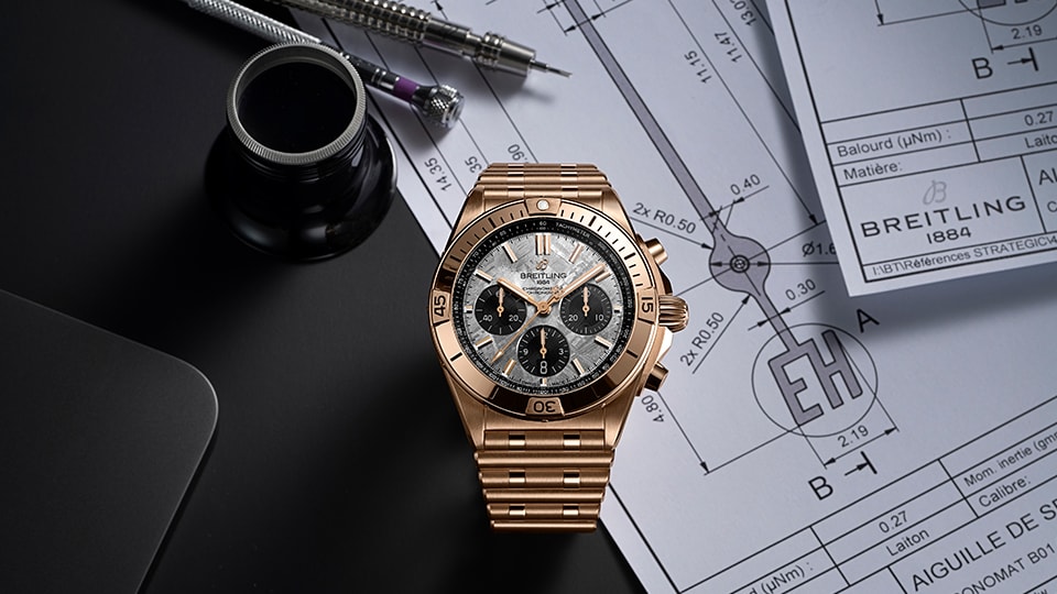 {generated} 技術図面上に置かれたローズゴールドのBreitling Chronomat Erling Haalandが精密工具とともに精度を強調