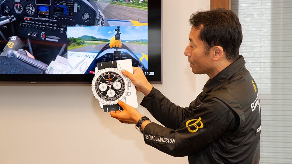 {generated} ブレイトリング装備のパイロットがブレイトリングナビタイマーディスプレイを手にし、Challenge Flightの操縦映像前で詳細を示している