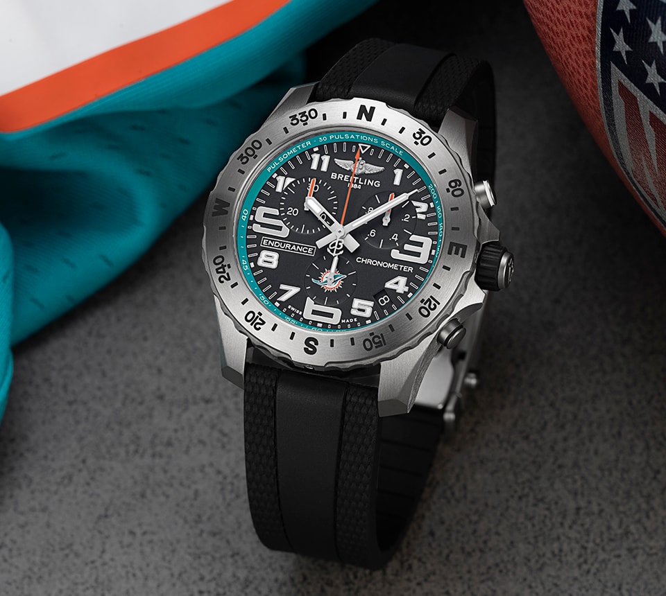 {generated} Breitling Endurance Pro腕錶以邁阿密海豚配色呈現，置於球隊裝備旁，展現鮮明的運動設計。