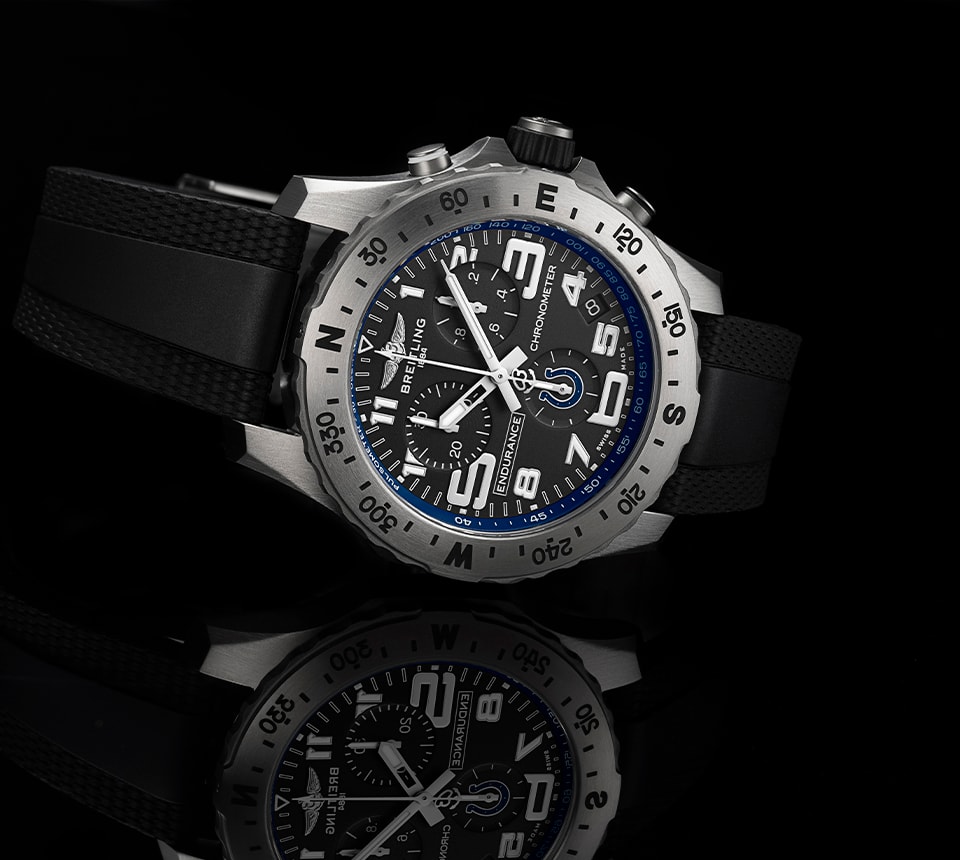 {generated} Breitling Endurance Pro watch with black strap and blue Colts detailing displayed on a reflective black surface