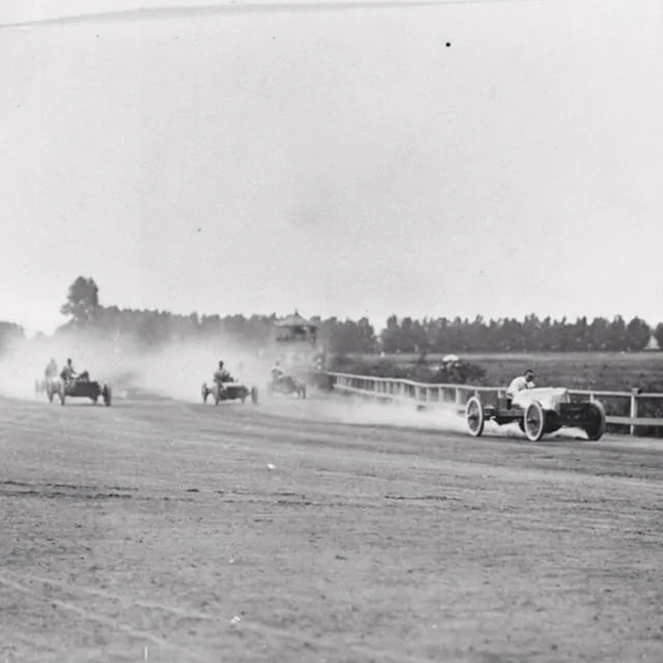 {generated} Vintage 1907 race cars speed along a dusty track, capturing early motorsport energy with drivers pushing toward the finish