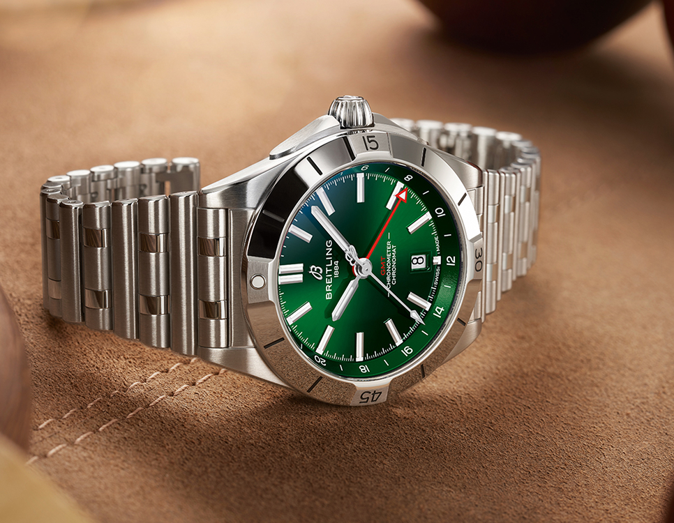 {generated} 緑のダイヤルを備えたBreitling Chronomatが、磨かれたスチールケースとブレスレットで温かみある革の上に置かれている。