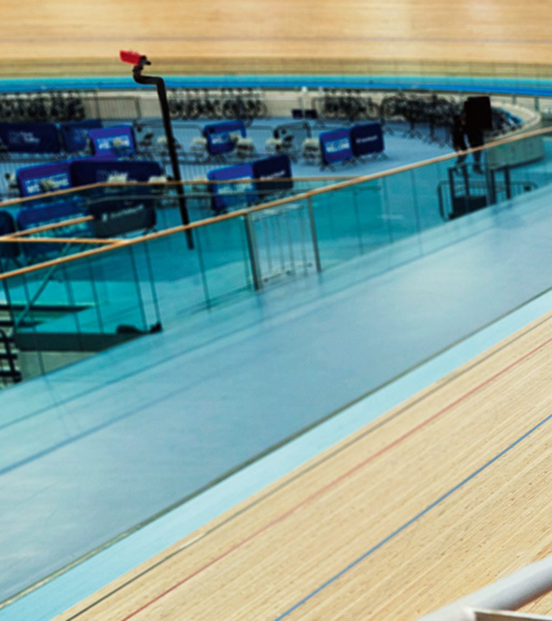 {generated} Man leaning on a velodrome railing wearing a Breitling sports watch with blue strap beside empty tiered seating.